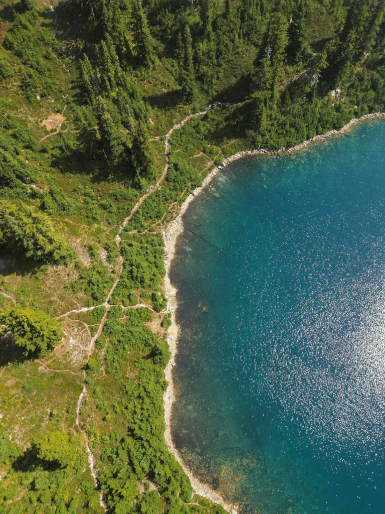 An aerial view of a pristine blue lake in Leavenworth, Washington, bordered by lush green forests and winding hiking trails, showcasing the area's natural beauty and outdoor appeal.