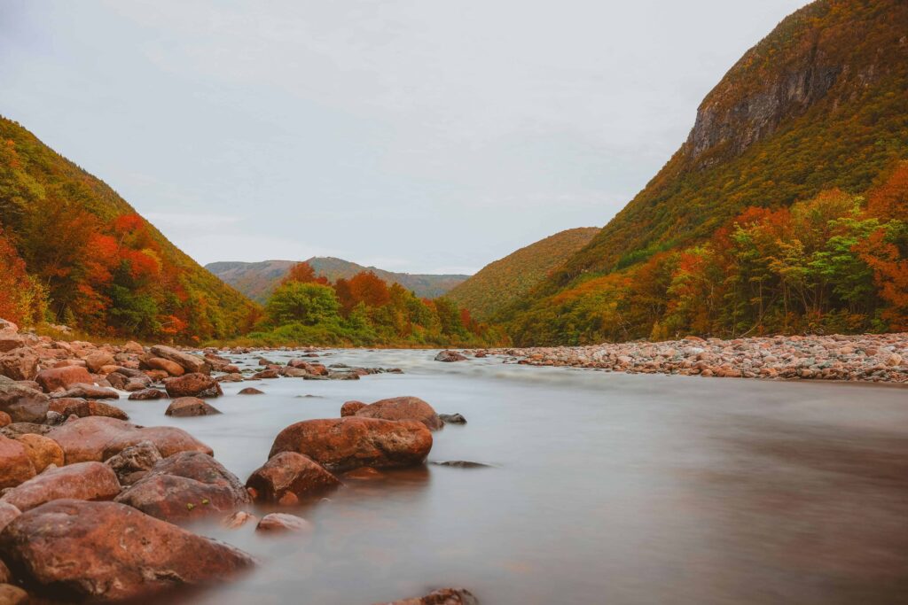 A serene river flowing through a picturesque valley with autumn-colored trees and rocky shores.