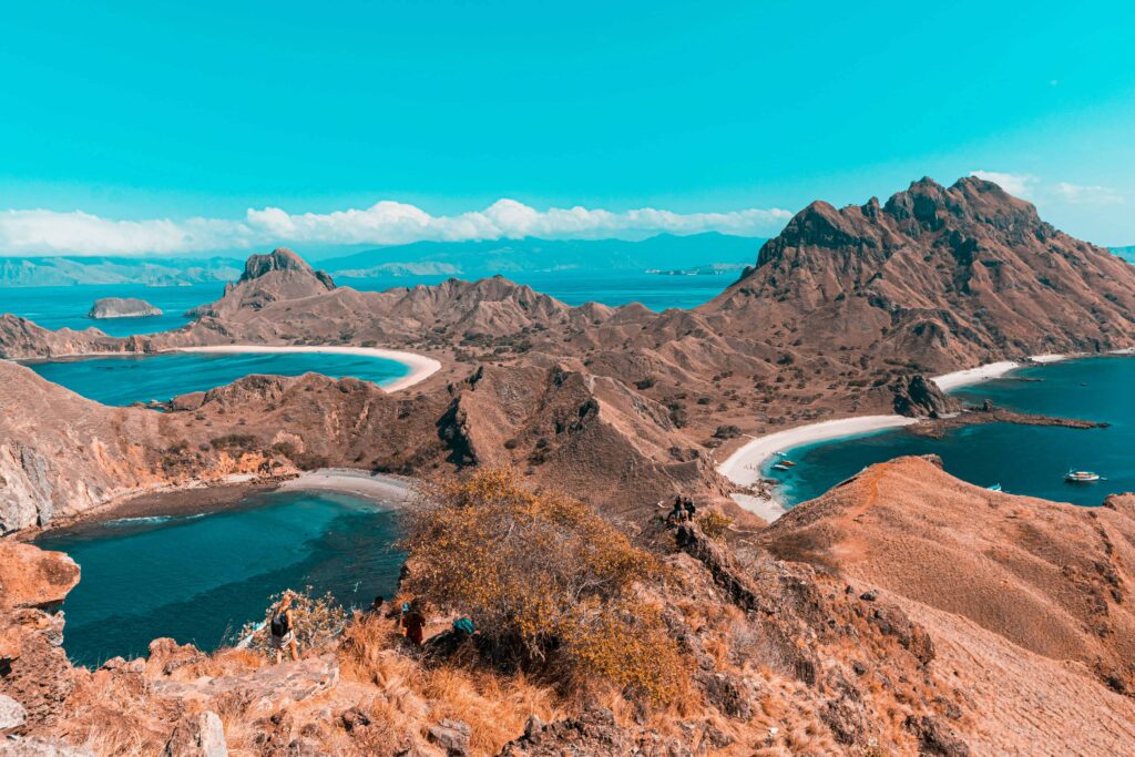 Stunning aerial view of Komodo Island's rugged landscape featuring a series of sandy bays and turquoise waters, with mountain peaks rising dramatically against a vibrant blue sky.