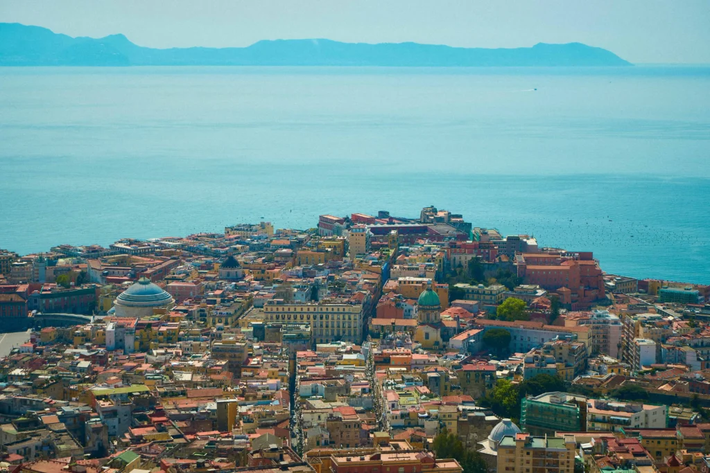 A panoramic view of Naples, Italy, highlighting the cityscape and the vast expanse of the Mediterranean Sea