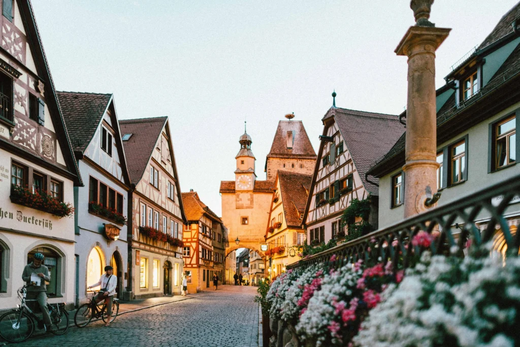 A quaint cobblestone street in a medieval European town, with timber-framed houses decorated with flowers and warm lighting.