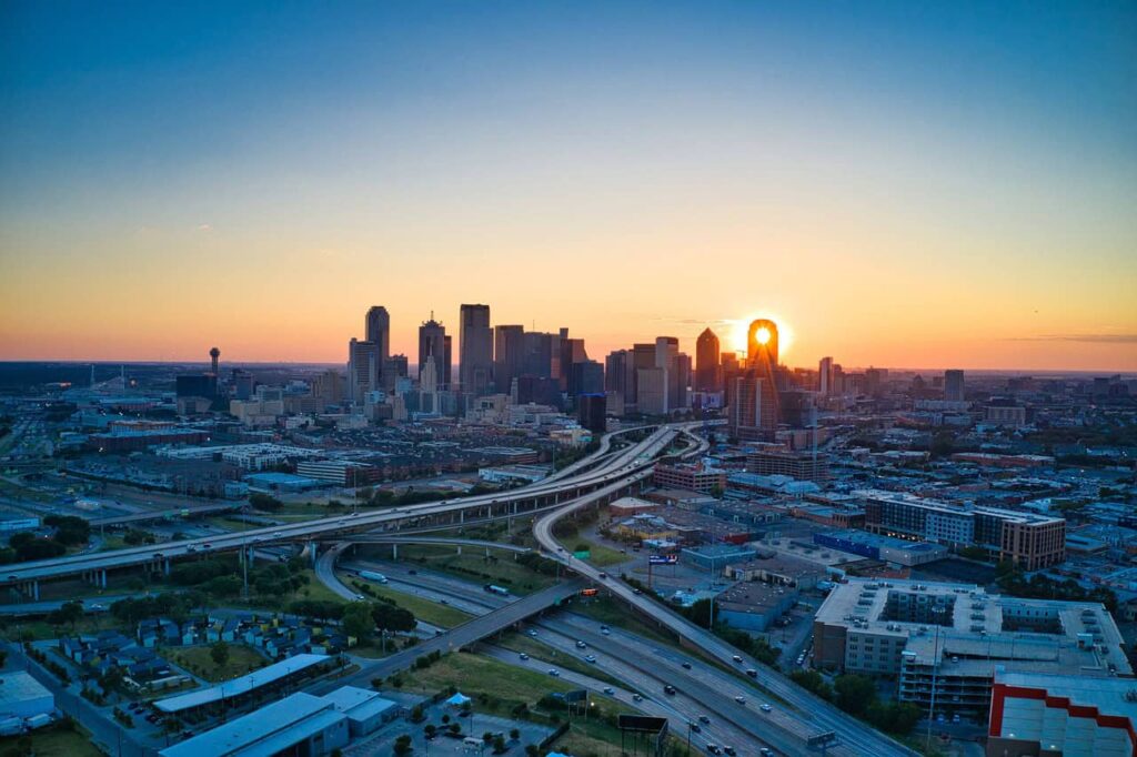 A stunning sunset over the Dallas skyline, with the sun setting behind the iconic buildings and highways weaving through the urban landscape