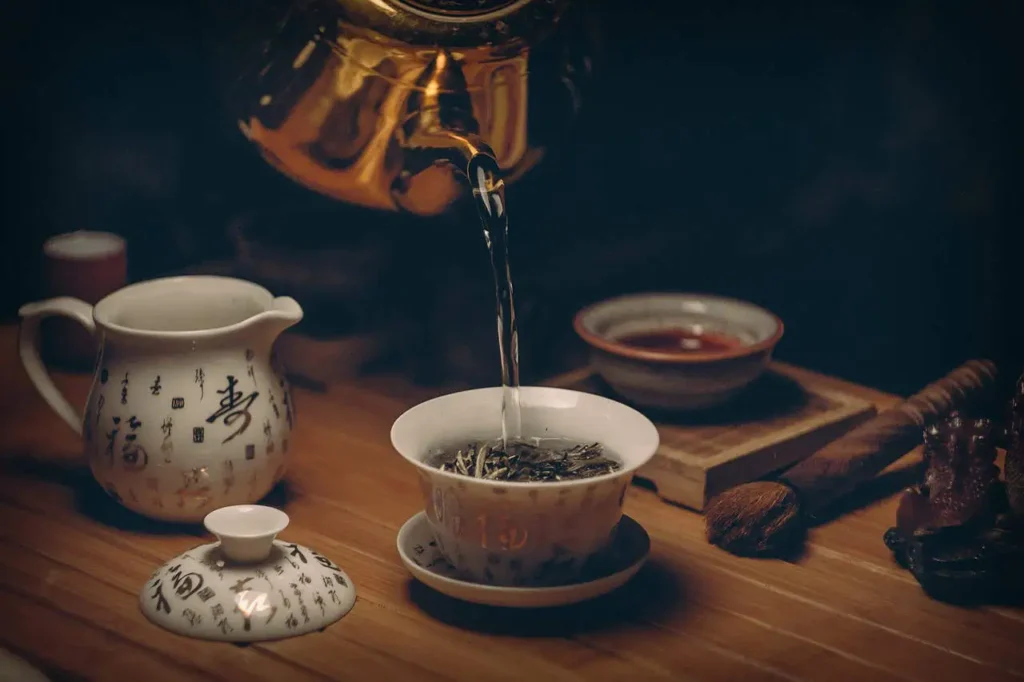 A close-up of traditional tea utensils, including a ceramic teapot and a gaiwan, with hot water being poured into the teacup, capturing the art of tea-making