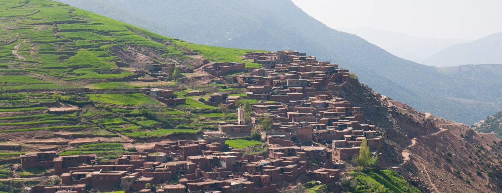 Breathtaking view of the Ourika Valley with terraced fields and traditional Berber houses nestled against the snow-capped Atlas Mountains.