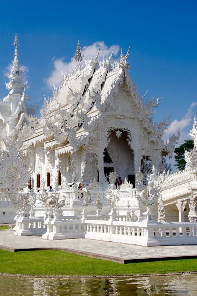 Close-up view of Wat Rong Khun, the White Temple in Thailand, showcasing the ornate and detailed white carvings against a clear blue sky.