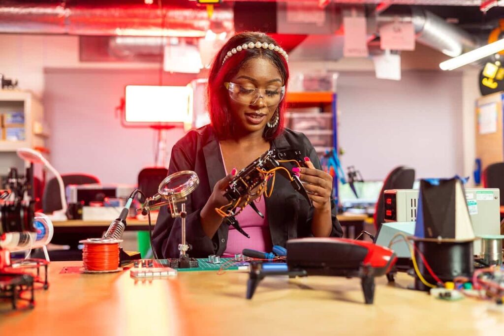 Young woman at Liberty Science Center's MakerSpace working on a robotics project, wearing safety glasses and using various electronic components, showcasing the hands-on learning opportunities available at Liberty Science Center.