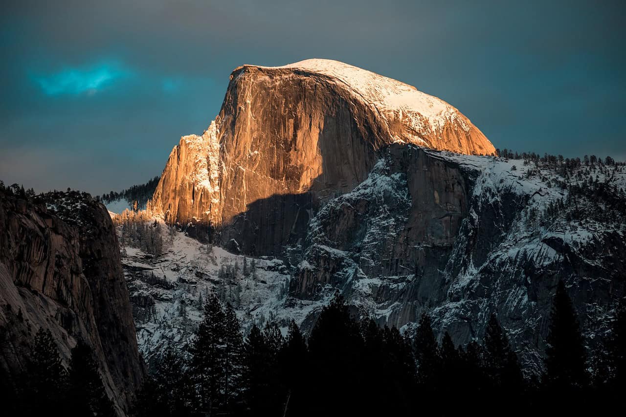 Half Dome in Yosemite National Park, one of the top 10 national parks to visit in the US in 2025, glowing under a sunset with snow-covered cliffs and towering pine trees, showcasing the park's breathtaking natural beauty.