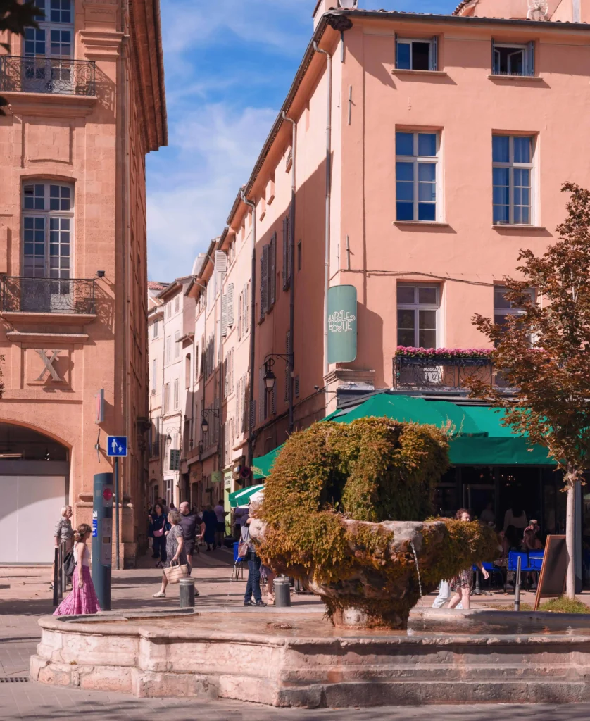 A picturesque street in Aix-en-Provence featuring pastel-colored buildings and a moss-covered fountain.