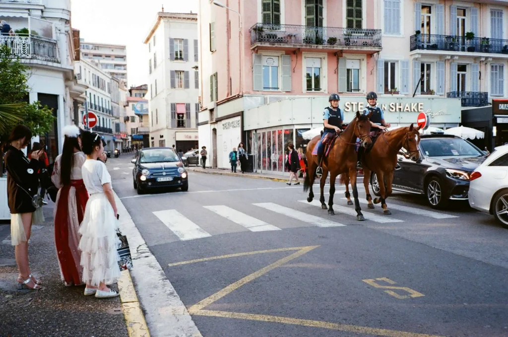 A lively street scene in Cannes France featuring mounted police officers and stylish pedestrians on a sunny day.