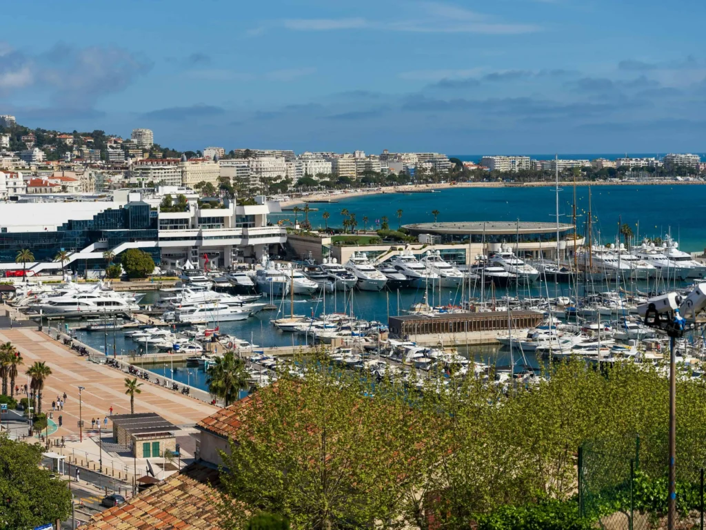 A panoramic view of the Cannes marina in the South of France, with rows of luxury yachts and a backdrop of elegant seaside buildings. The bright blue waters epitomize the coastal charm of the French Riviera