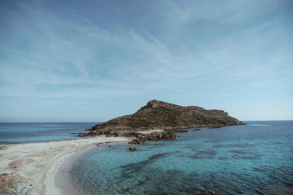 A serene coastal landscape featuring a rocky island surrounded by crystal-clear turquoise waters and a sandy shoreline under a vast blue sky.