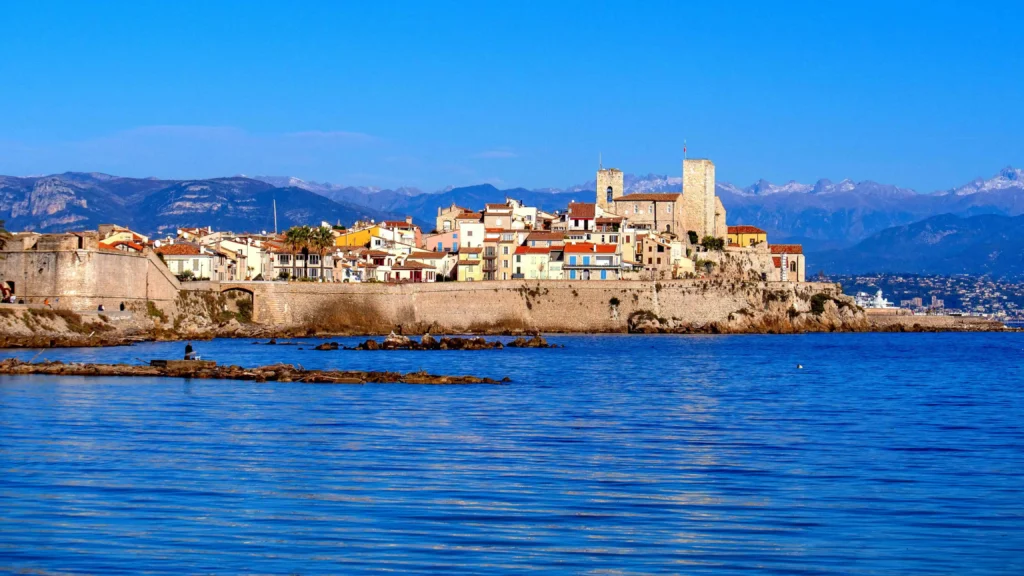 A panoramic view of Antibes with its historic fortress, colorful buildings, and distant mountains.