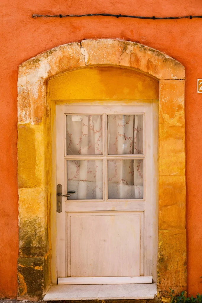 A charming, brightly colored door with a rustic stone frame, set in an orange and yellow wall in France