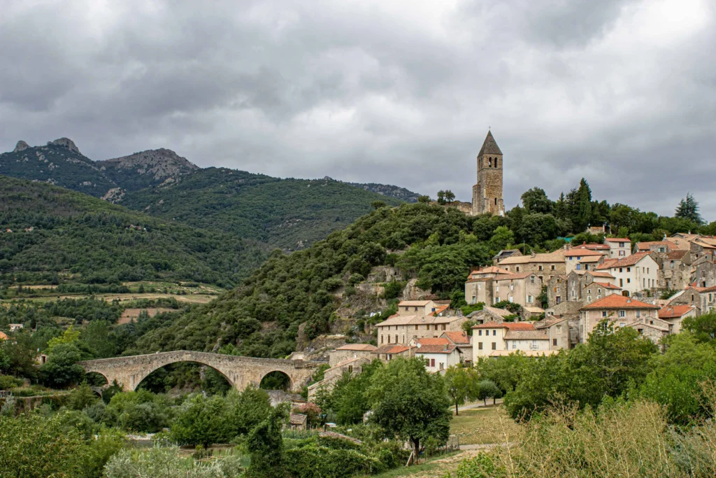 A picturesque Languedoc village set against a backdrop of rolling hills, featuring a historic church and an arched stone bridge in provence south of france