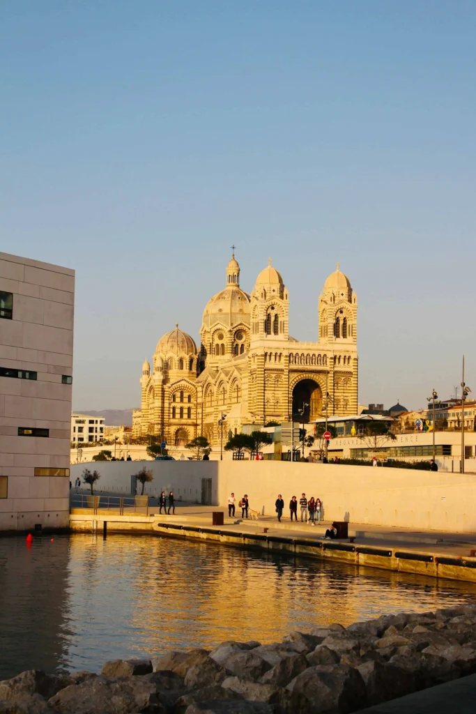 The stunning Marseille Cathedral with its unique striped architecture, glowing in the golden hour light, reflected in the water nearby.