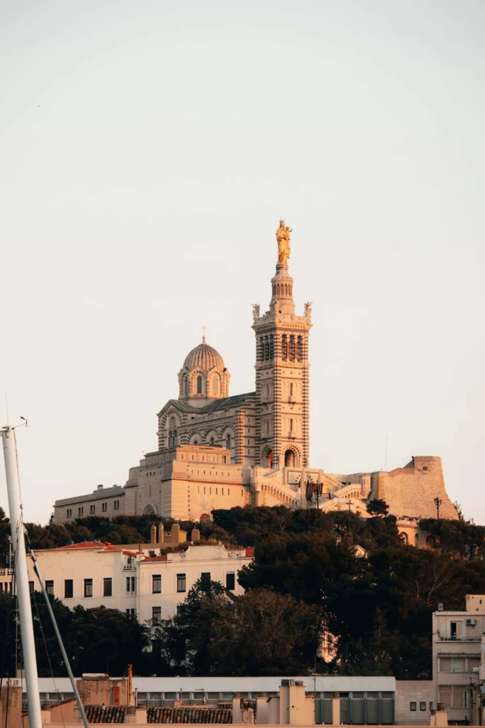 The majestic Basilica of Notre-Dame de la Garde in Marseille, glowing warmly at sunset with its iconic golden statue on top.