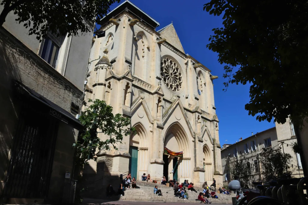 A Gothic-style church facade with a large rose window, basking in sunlight as visitors gather on the steps.