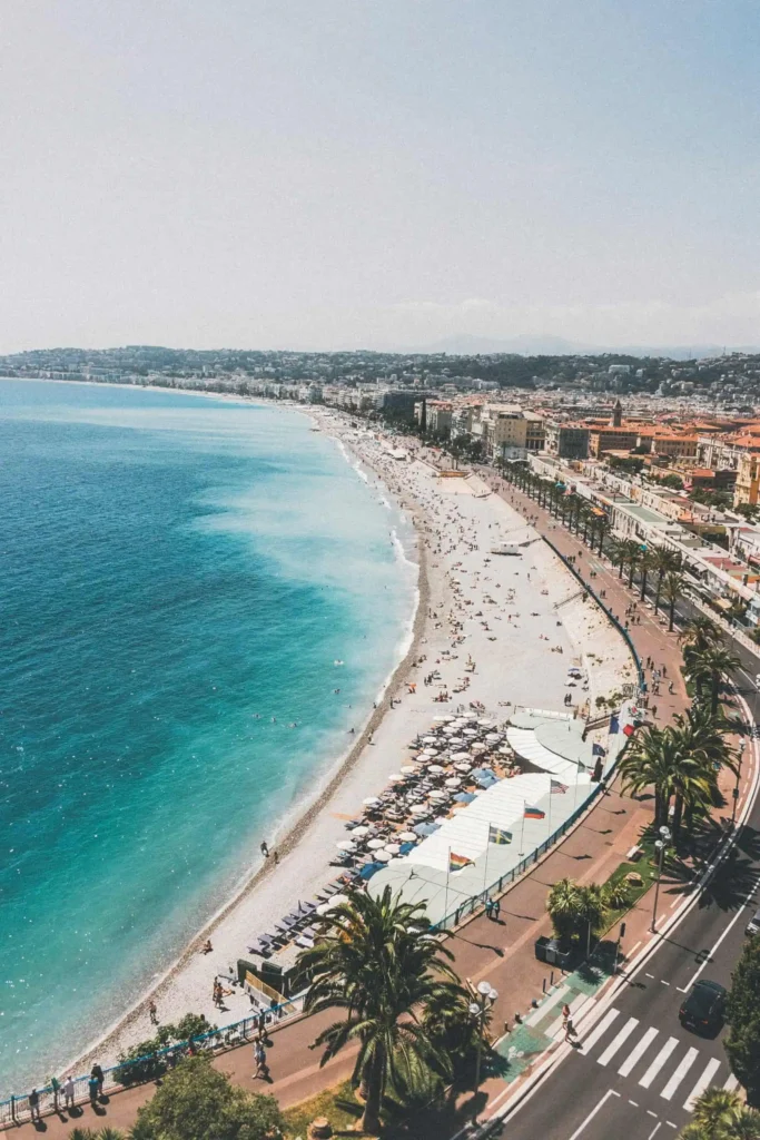 A scenic aerial view of Nice's Promenade des Anglais and pebbled beach, with azure waters and bustling city life in France