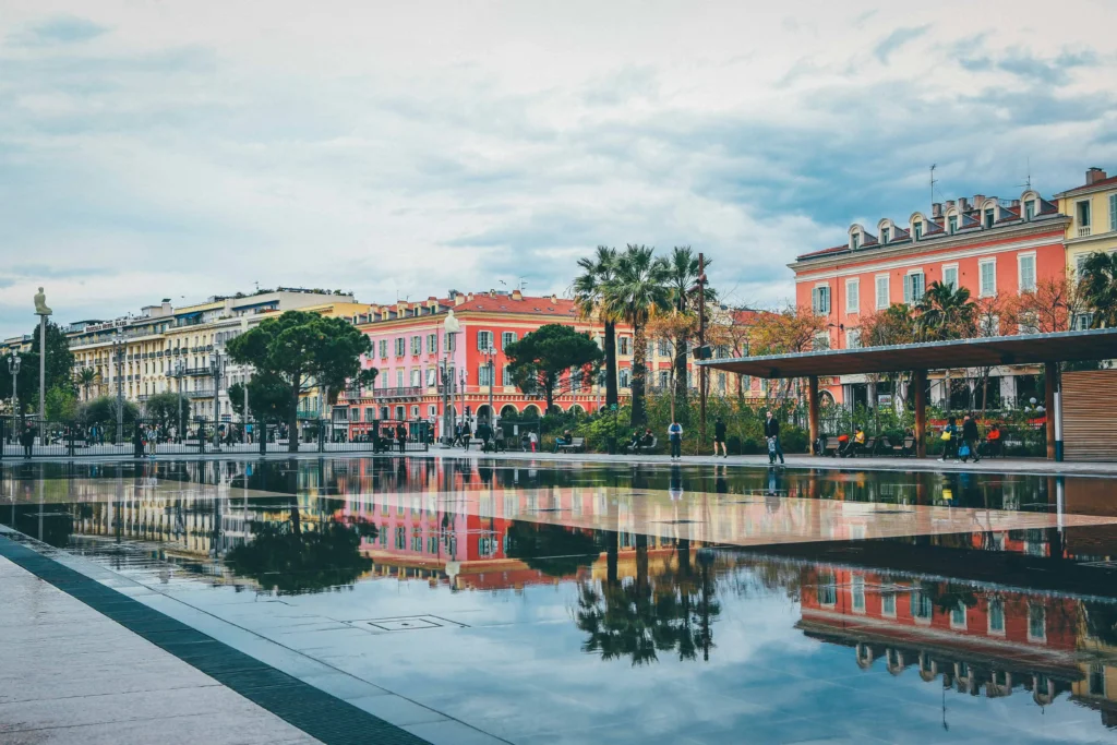 Vibrant buildings reflected in the square in Nice, with palm trees and a peaceful ambiance.