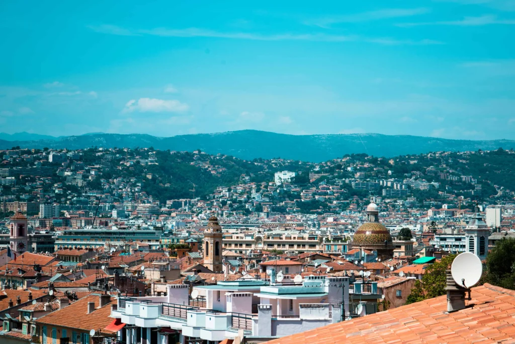 Cityscape of Nice South France, with terracotta rooftops and green hills under a clear blue sky.