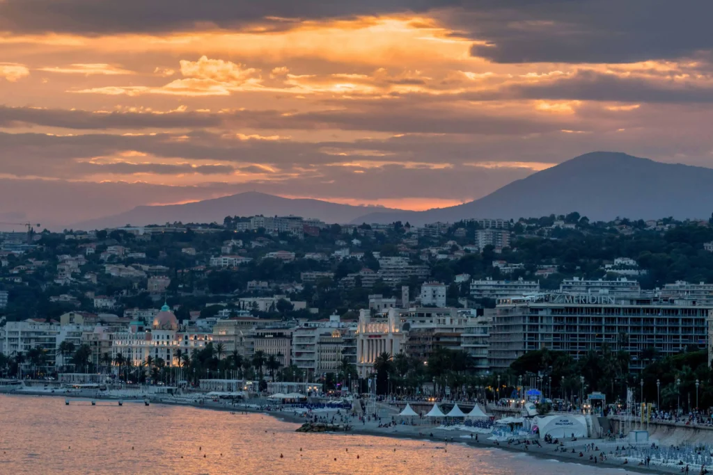 The scenic coastline of Nice France at sunset, with a view of the cityscape and mountains in the background.
