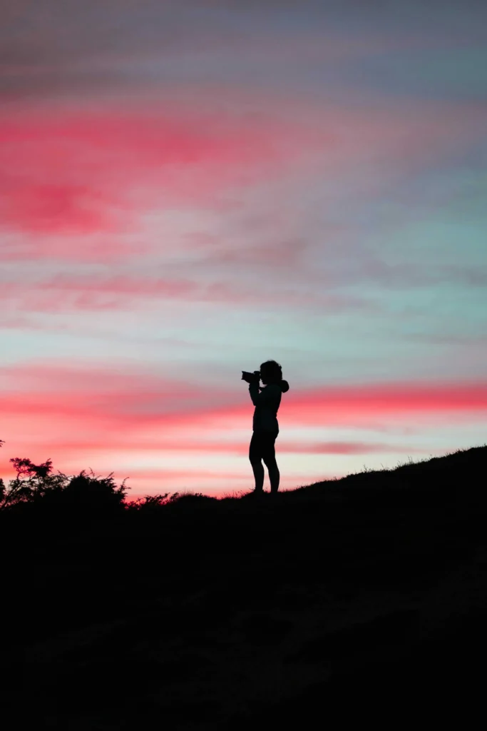 A silhouette of a person with a camera capturing the stunning pink and blue hues of a vibrant sunset in south of france