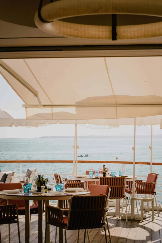 A breezy coastal dining area with tables set under a white canopy, overlooking a calm blue sea and distant islands in provence south of france