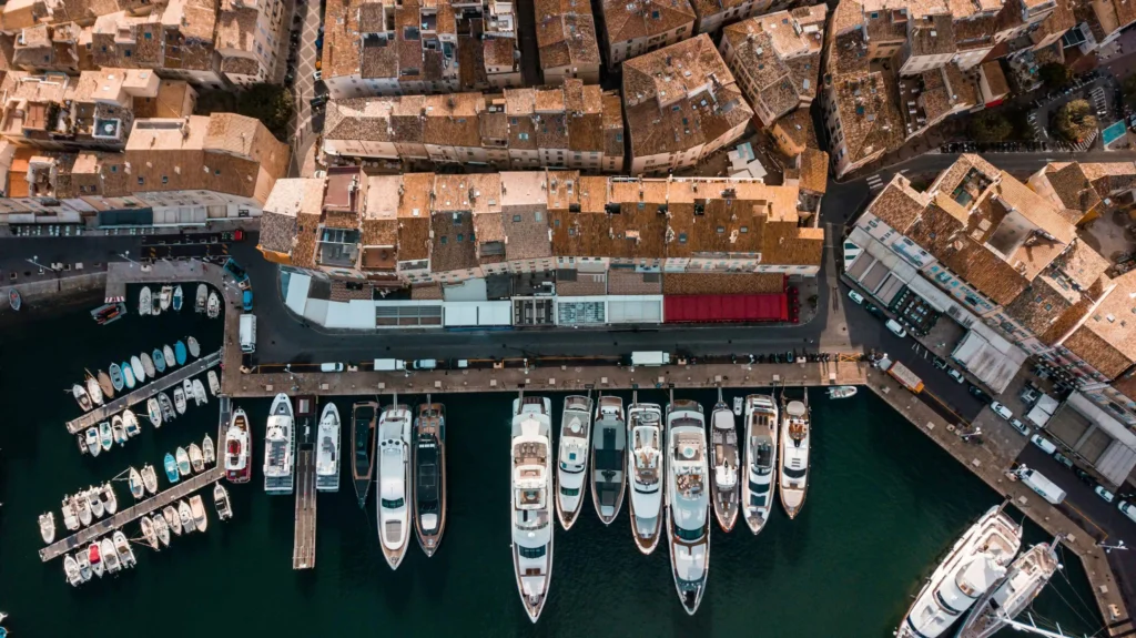 A detailed bird's-eye view of a marina with yachts docked along rows of terracotta-roofed houses.