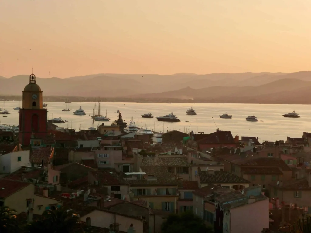 The picturesque town of Saint-Tropez at sunset, with sailboats and yachts anchored in the bay and the iconic bell tower in the foreground in France