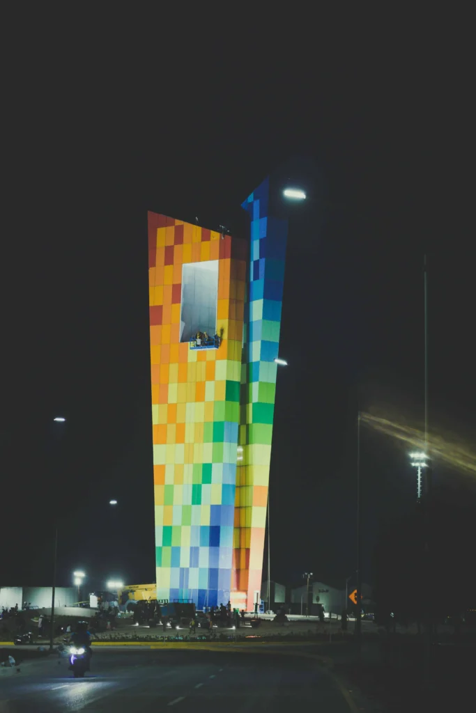 A modern rainbow-colored tower in Colombia illuminated at night, with vibrant hues creating a striking urban landmark against the dark sky