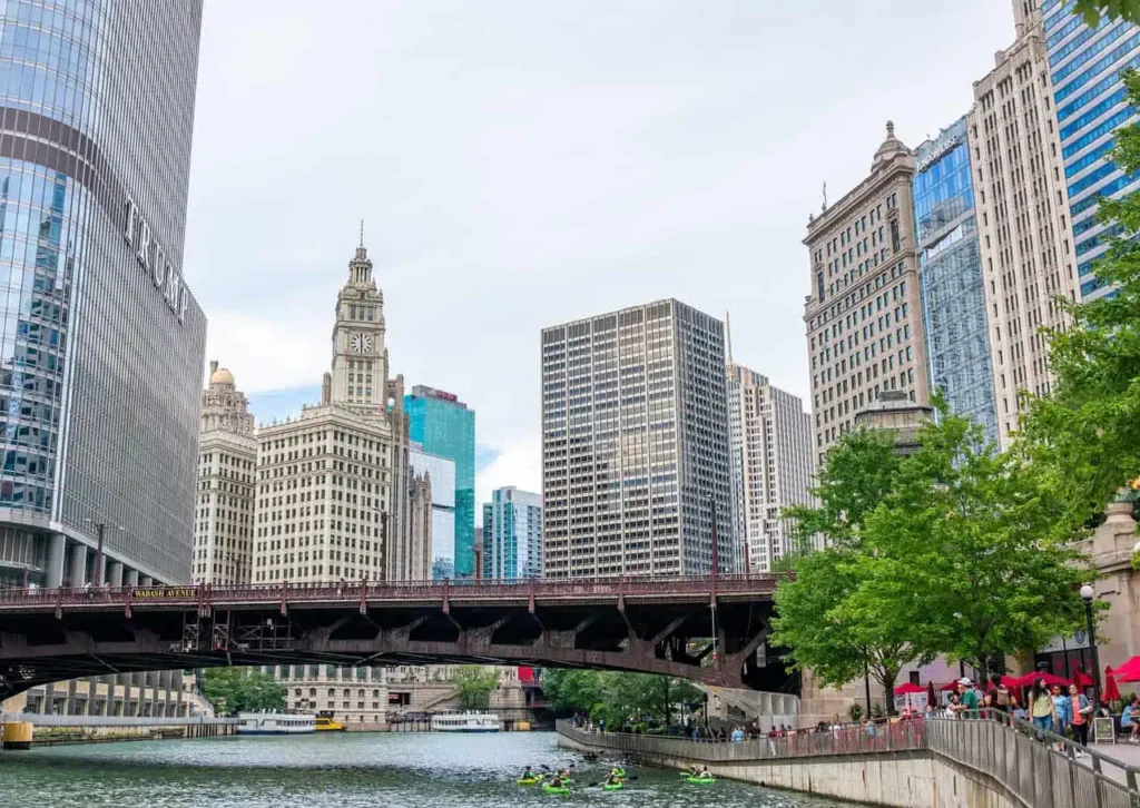  A vibrant view of the Chicago Riverwalk with iconic buildings and a busy bridge in the foreground.