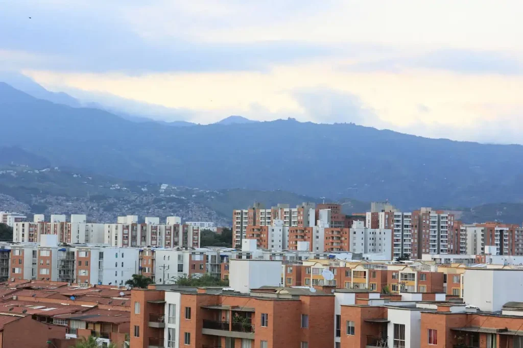 A cityscape of Cali, Colombia, featuring modern apartment buildings and the Andes mountains in the background under a tranquil cloudy sky.