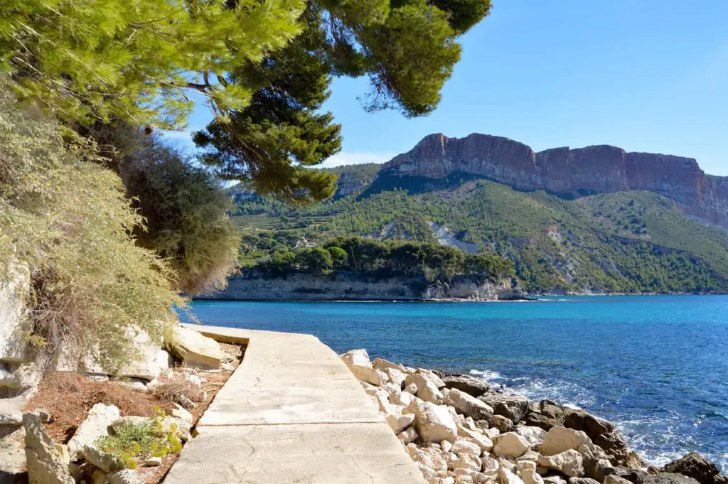 Serene walking path along the Mediterranean coast with turquoise waters and lush greenery.