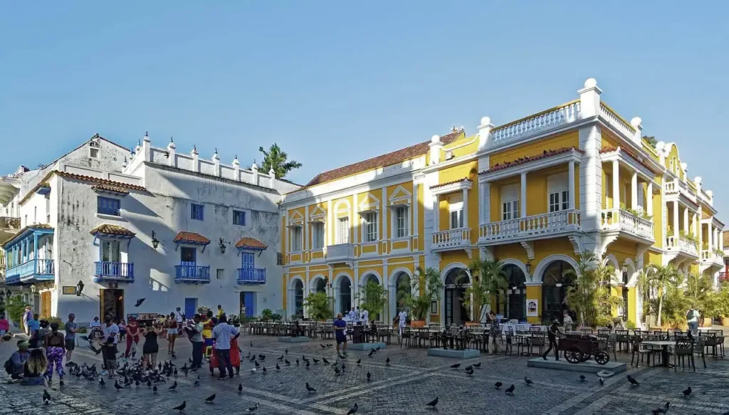 The colorful and historic plaza in Cartagena, Colombia sa, with yellow colonial buildings, a bustling crowd, and pigeons in the foreground
