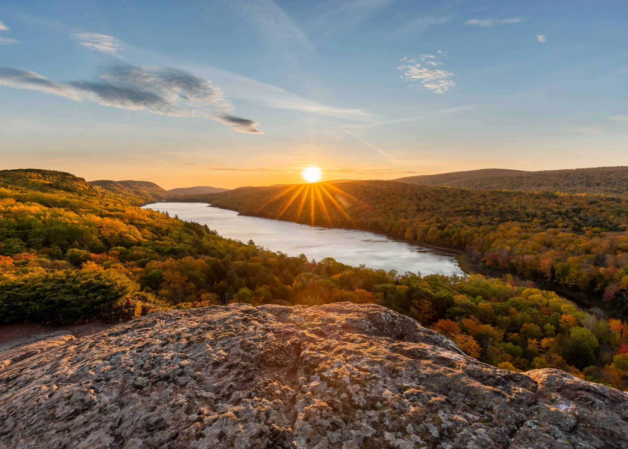 A serene sunrise over Lake of the Clouds in Michigan, casting golden light across the water and illuminating the surrounding vibrant autumn foliage.