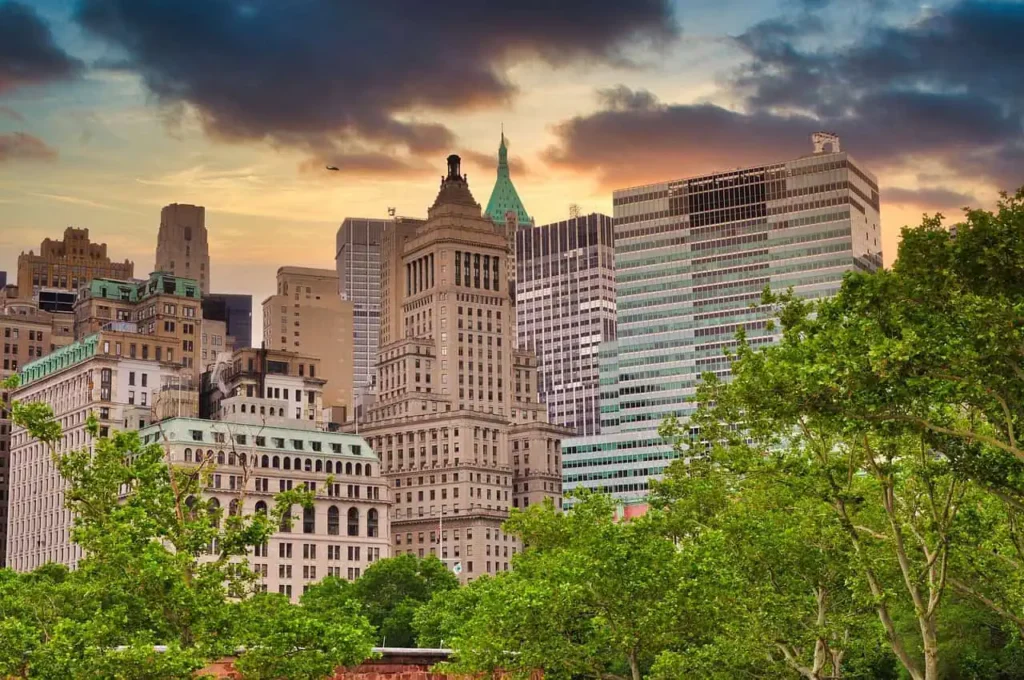 Skyline of Lower Manhattan at sunset, featuring historic and modern buildings with a colorful sky backdrop.