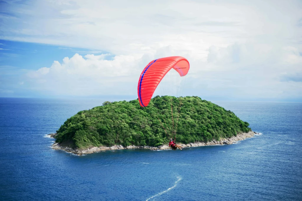 A person parasailing over a lush green island surrounded by the blue ocean in Thailand.