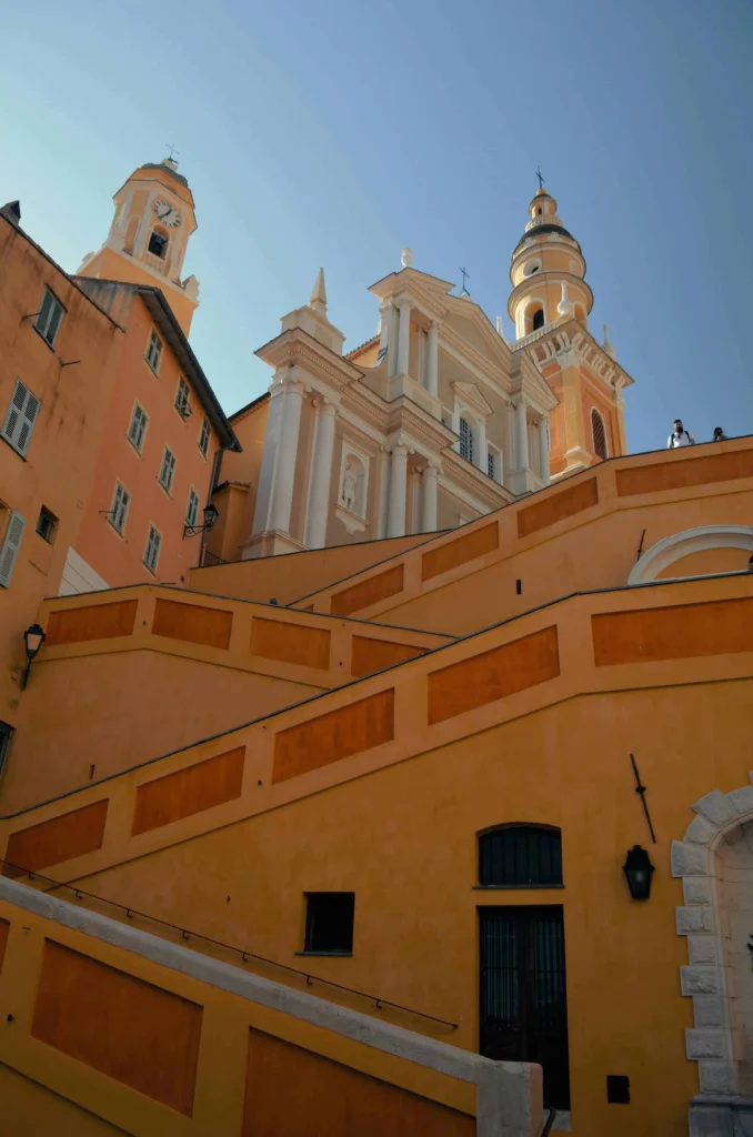 Close-up of Menton's historic architecture, featuring the Basilica of Saint-Michel-Archange with its yellow and white facade and surrounding orange-toned buildings.