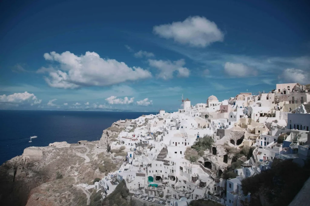 A panoramic view of Oia's iconic whitewashed buildings and windmills under a clear blue sky in Santorini, Greece. (Keyphrase: Santorini Greece Honeymoon)