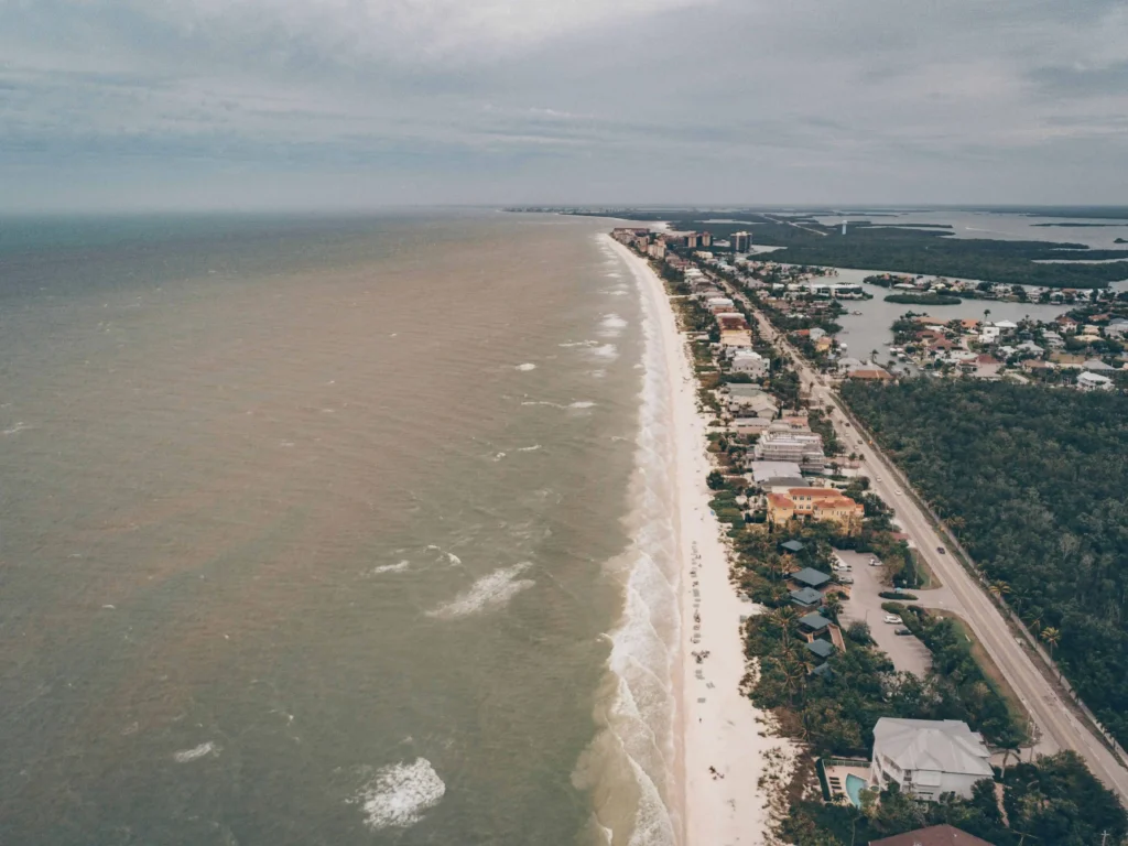 Aerial view of luxurious homes and canals along the coastline of Naples, Florida, bordered by turquoise waters and beaches.