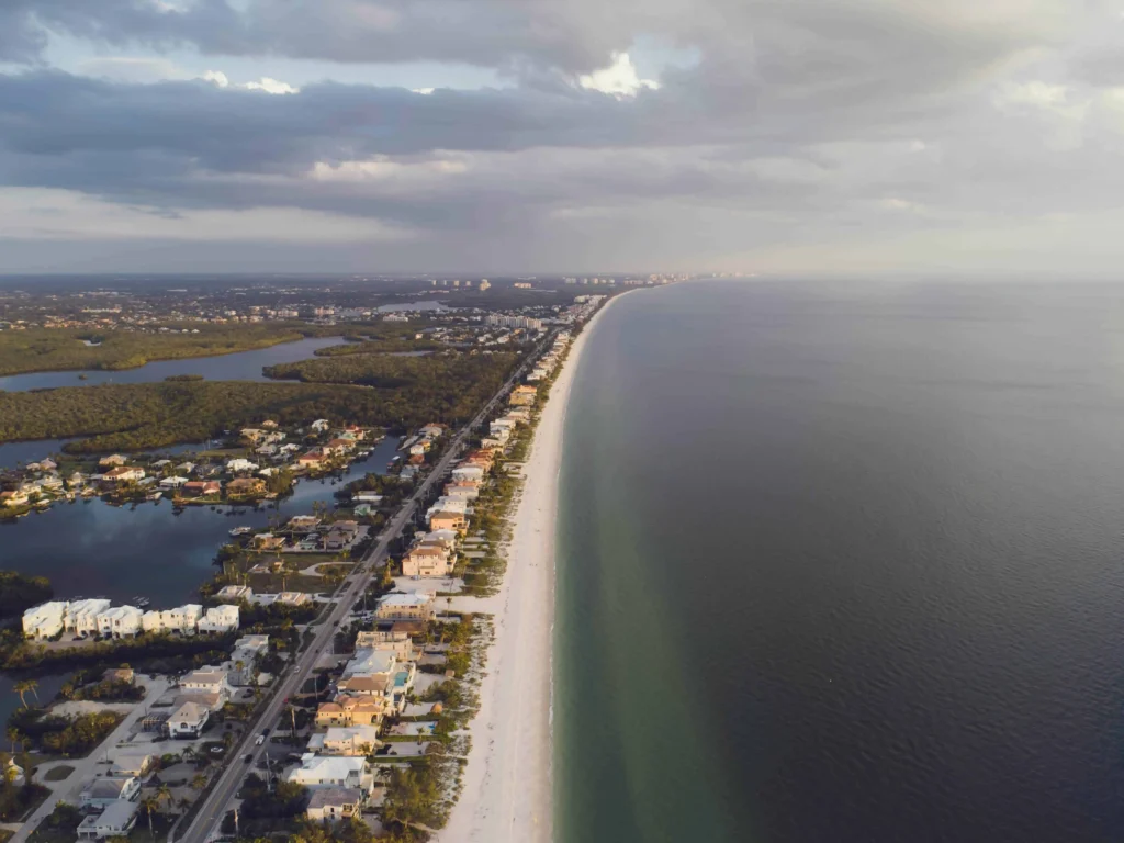 Aerial view of luxurious homes and canals along the coastline of Naples, Florida, bordered by turquoise waters and pristine beaches.