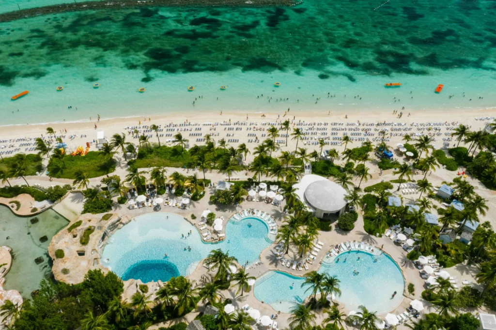 Aerial view of a resort in Nassau featuring multiple swimming pools, palm trees, and a beach with clear turquoise water.