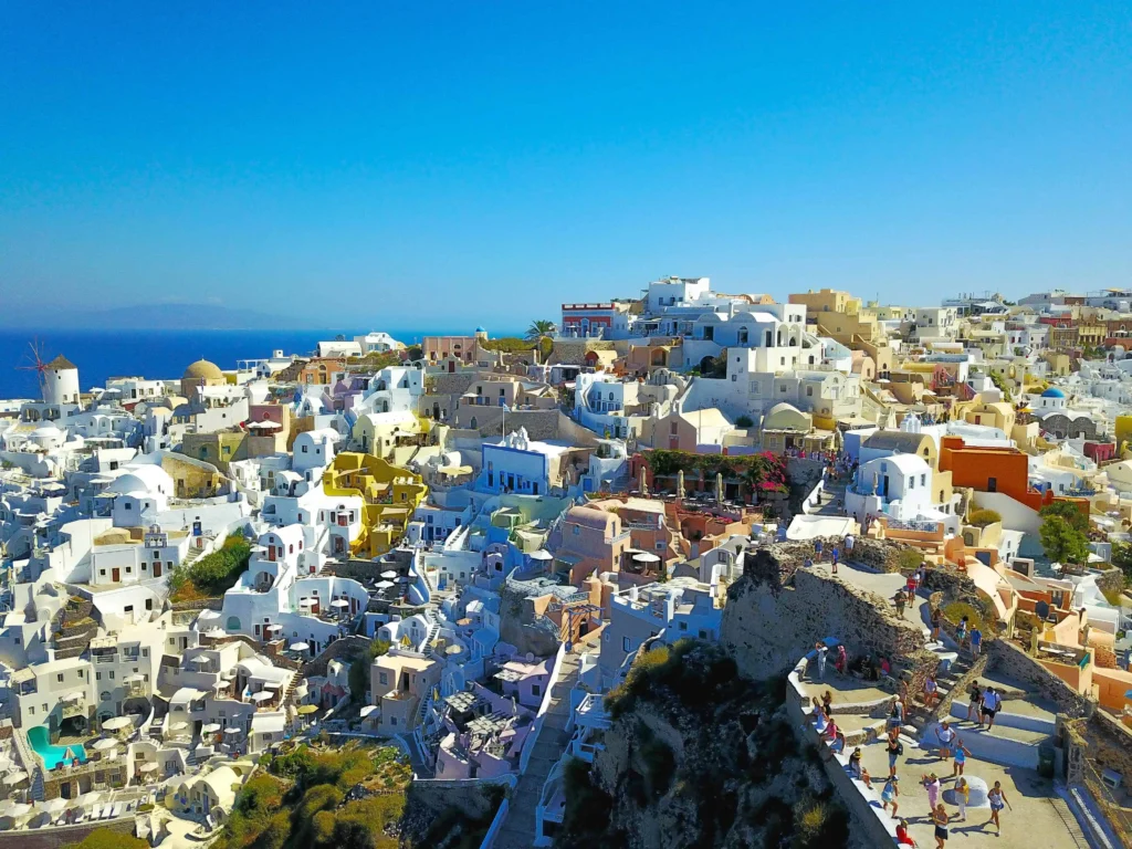 A colorful aerial view of Oia's narrow streets and iconic architecture under the bright Mediterranean sun. 