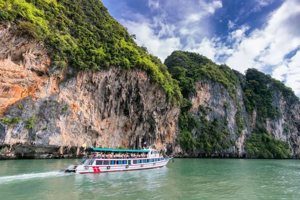 Boat cruising along limestone cliffs surrounded by green waters in Thailand.