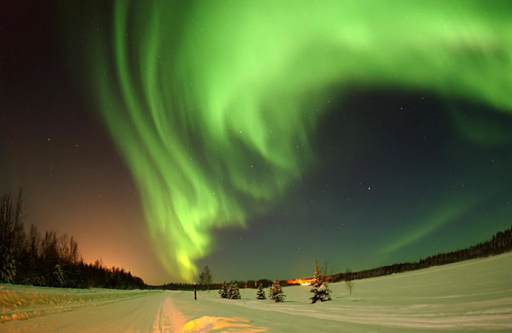 The Northern Lights glowing brightly in green hues above a snow-covered landscape, a must-see attraction in things to do in Fairbanks Alaska.