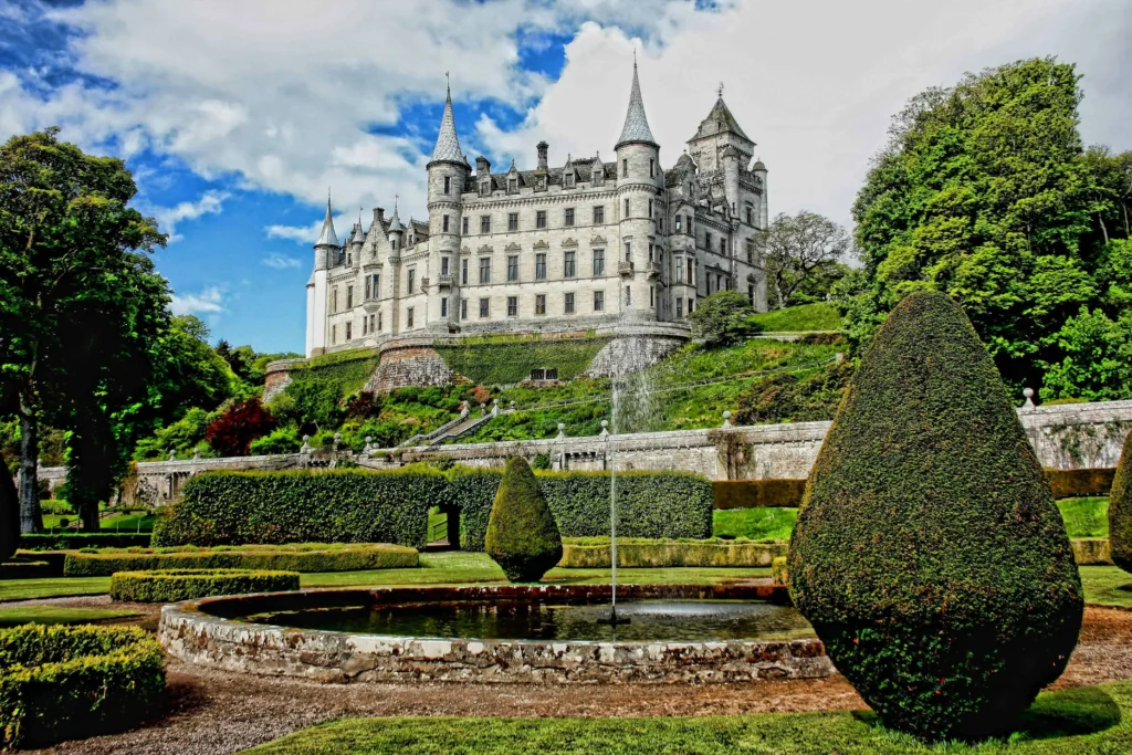 Dunrobin Castle surrounded by lush green gardens, vibrant trees, and a clear blue sky in the background.