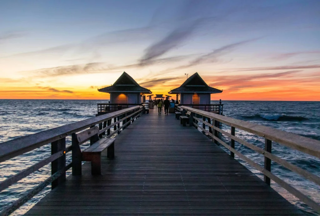 A breathtaking view of the Naples Pier at sunset, with visitors silhouetted against a vibrant orange and pink sky