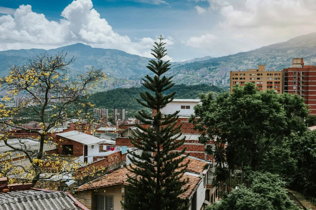 A scenic view of Medellín, Colombia sa showcasing residential areas with lush greenery, blooming yellow trees, and distant mountains under a partly cloudy sky.