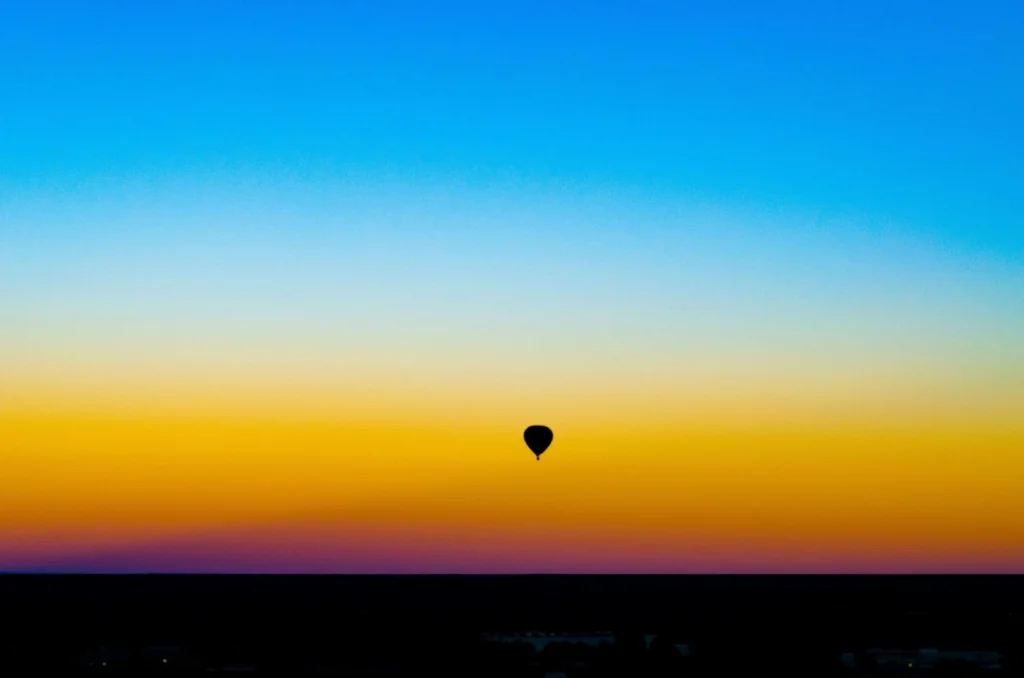 A silhouette of a hot air balloon drifting against a gradient sunset sky that transitions from deep blue to warm orange.