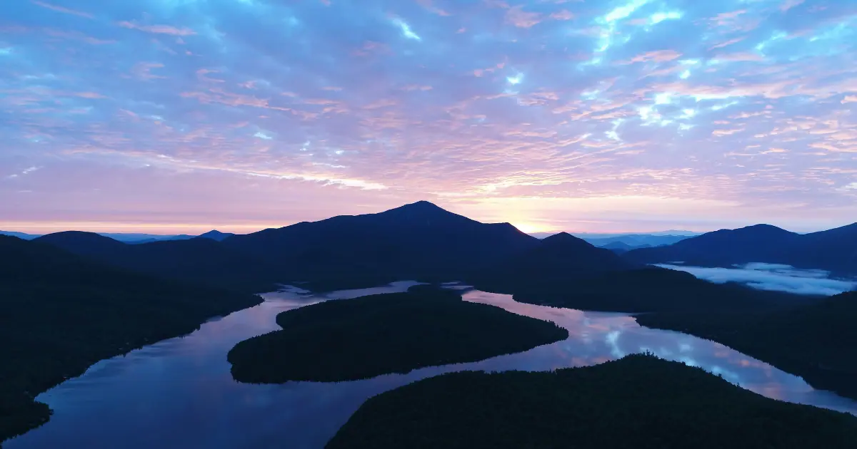 A mesmerizing sunrise over Lake Placid with the silhouette of mountains and a serene lake view.